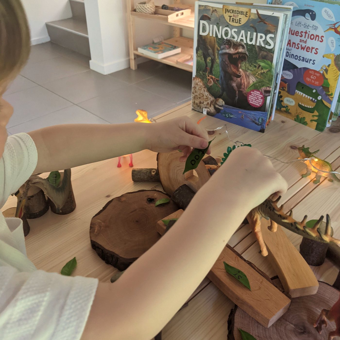 A child playing with dinosaurs and word leaves on a wooden small-world table