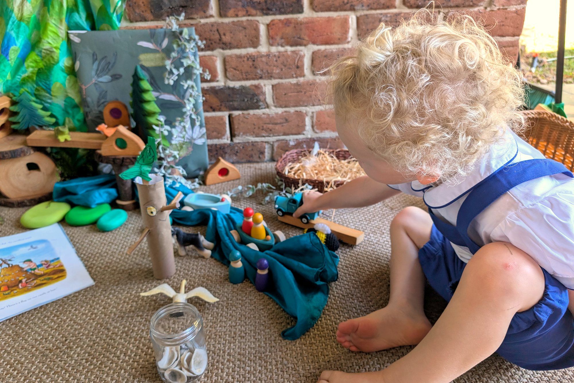 A toddler playing with wooden toys and a small world set-up at home