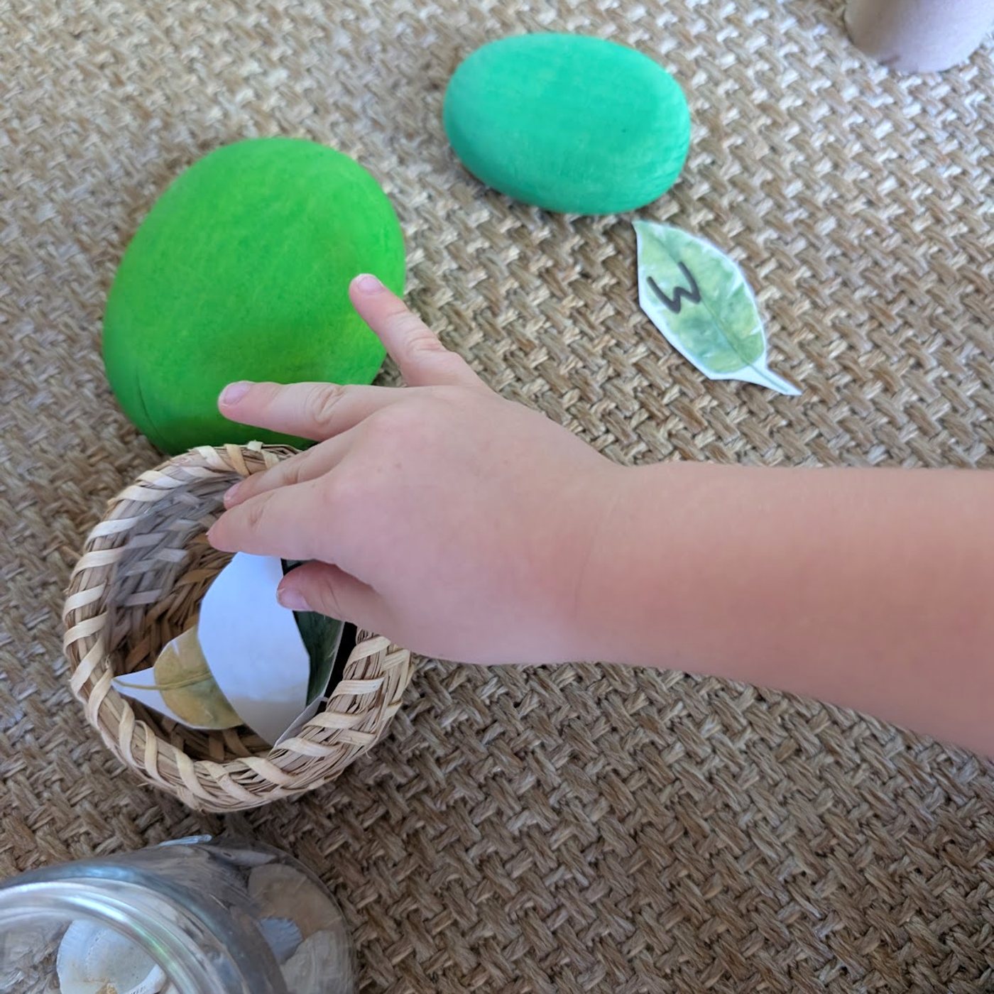 A child’s hand choosing a letter leaf from a little basket during reading play