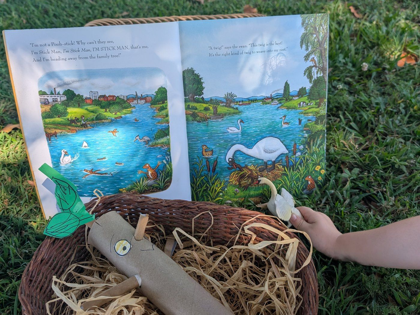 Open picture book on the grass with a cardboard stick man in a basket